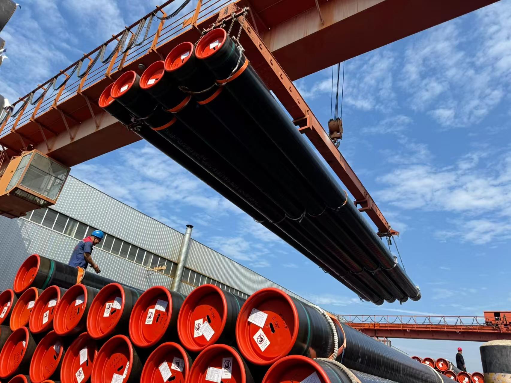 Large-diameter steel pipes lifted by overhead crane in the yard